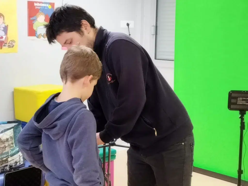 Gwenolé Robert installant un micro à un élève lors d'un atelier vidéo sur fond vert.