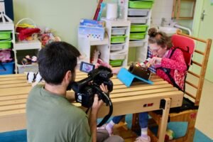 Un vidéaste filmant de dos un enfant handicapé lors d'une séance d'éducation conductive à l'association Honorine lève toi.