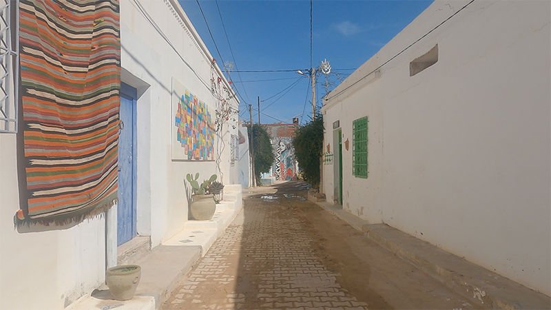 Une rue colorée du quartier Djerbahood à Djerba, ornée de fresques de street art, illustrant la fusion entre tradition tunisienne et art contemporain.