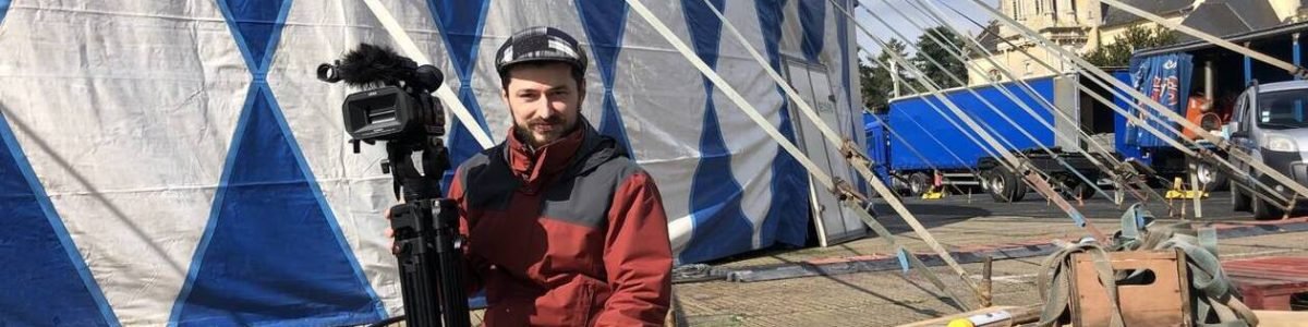 Vidéaste posant avec sa caméra devant le chapiteau du Festival International de Cirque de Bayeux 2023